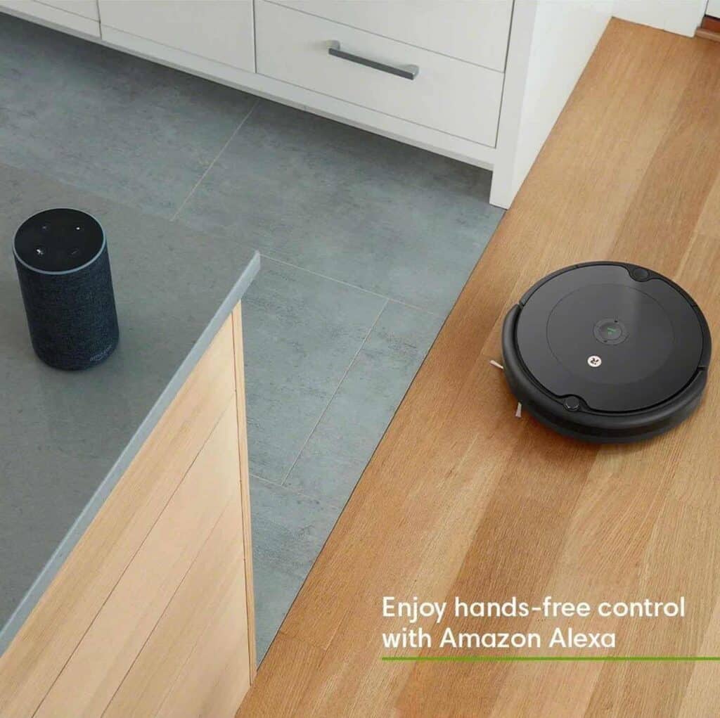 A roomba 694 robotic vacuum cleaner is next to a wooden floor in a kitchen.